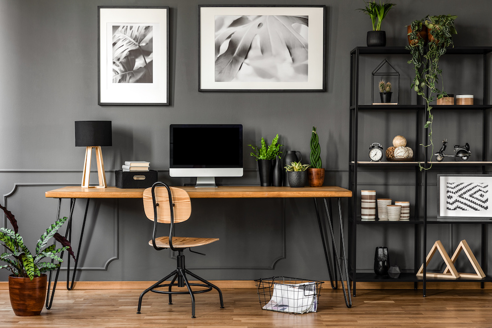 Posters on grey wall above wooden desk in natural home office interior with plants and lamp